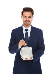 Young businessman putting money into piggy bank on white background