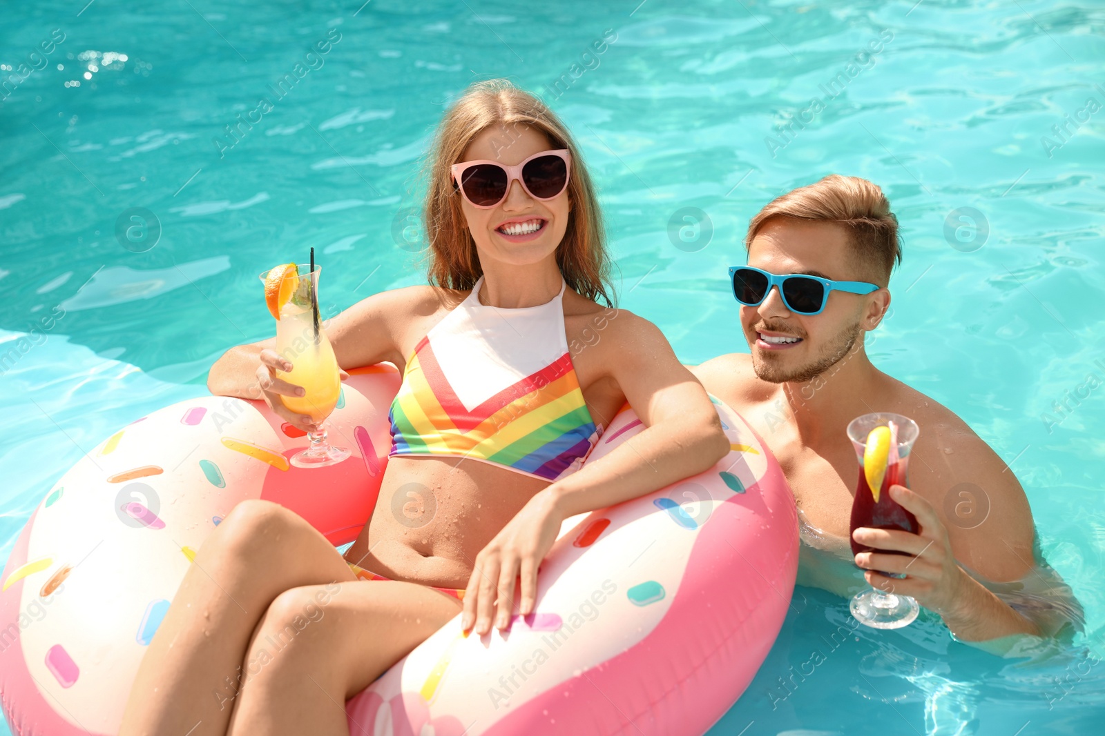 Photo of Young couple with cocktails in pool on sunny day