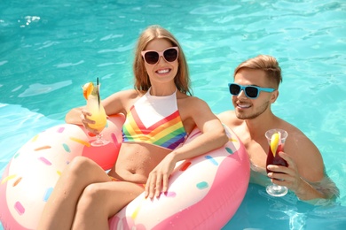 Young couple with cocktails in pool on sunny day