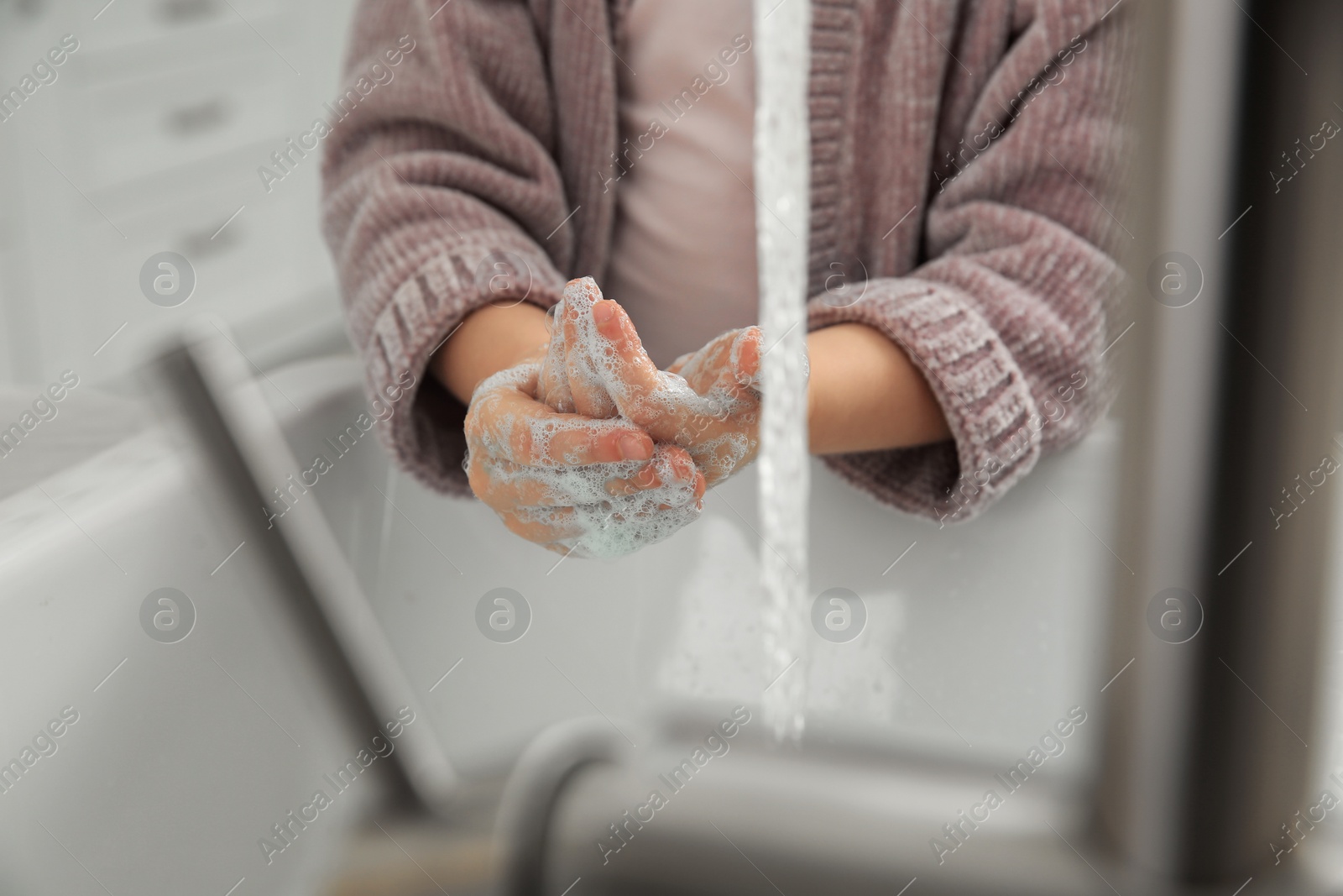Photo of Little girl washing hands with liquid soap at home, closeup