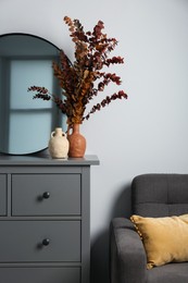 Photo of Grey chest of drawers with decor and armchair near white wall in room. Interior design