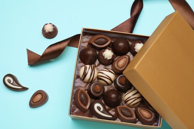 Open box of delicious chocolate candies on light blue background, flat lay