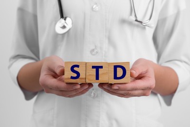 Photo of Doctor holding wooden cubes with abbreviation STD on white background, closeup