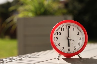 Photo of Red alarm clock on table outdoors at sunny morning. Space for text