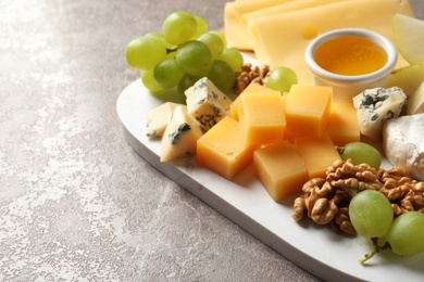 Photo of Board with different kinds of delicious cheese and snacks on marble background