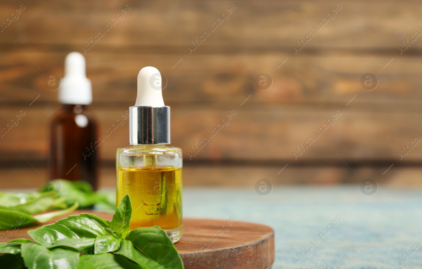 Photo of Wooden board with glass bottle of oil and basil leaves on table. Space for text