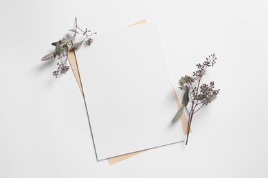 Photo of Empty sheet of paper and decorative eucalyptus leaves on white background, flat lay. Mockup for design