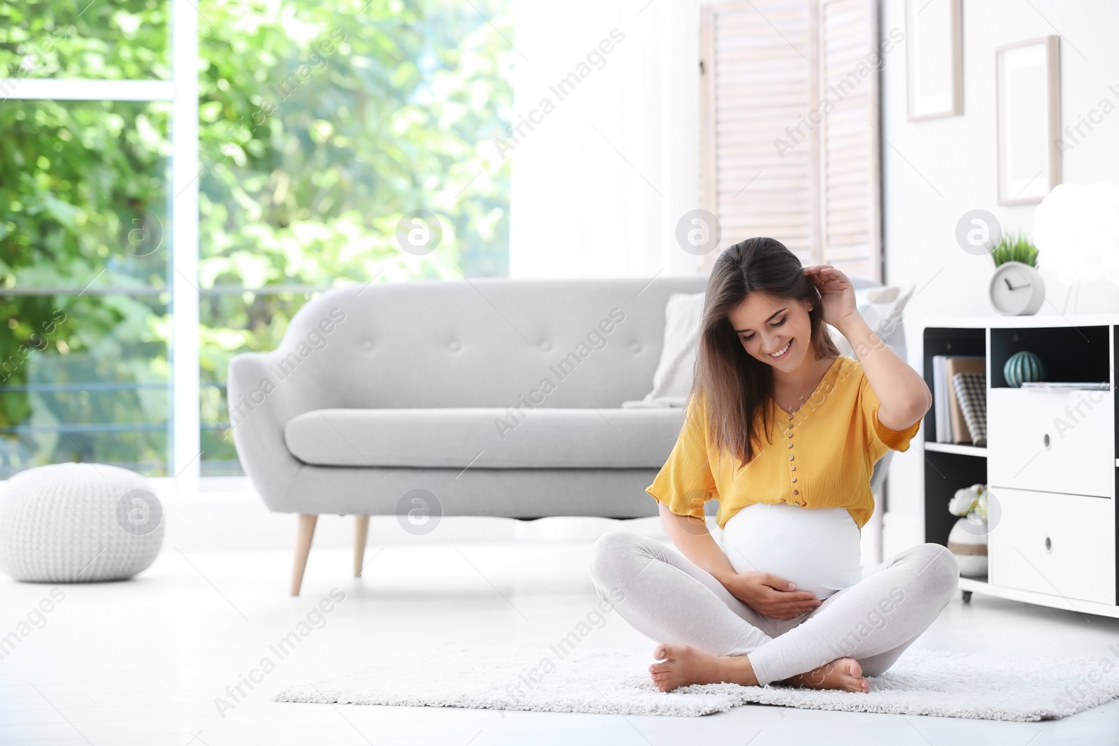 Photo of Happy pregnant woman sitting on floor at home