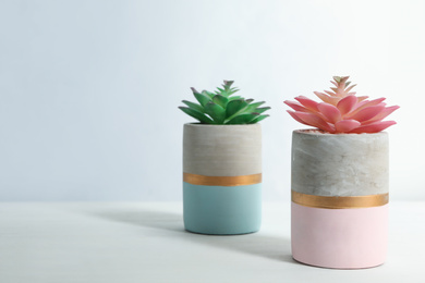 Artificial plants in flower pots on white wooden table. Space for text