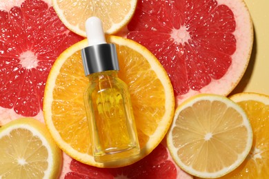 Photo of Bottle of cosmetic serum and sliced citrus fruits on yellow background, flat lay