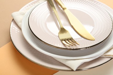 Ceramic plates, cutlery and napkin on color background, closeup