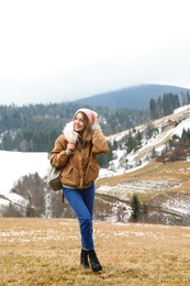 Young woman in warm clothes near snowy hill. Winter vacation