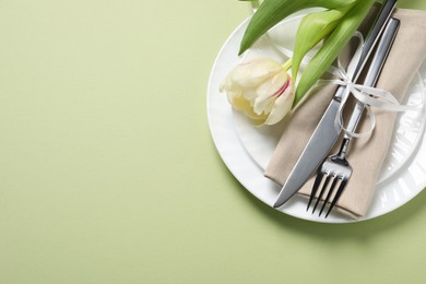 Stylish table setting with cutlery and tulip on light green background, top view. Space for text