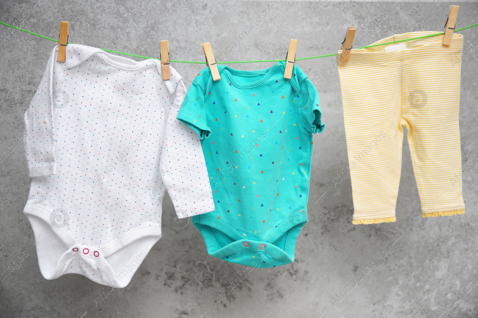 Photo of Baby clothes hanging on washing line against gray background