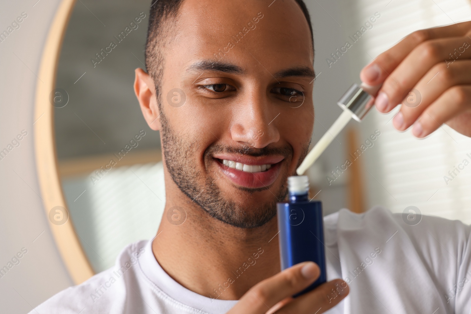 Photo of Handsome man with cosmetic serum in hands indoors