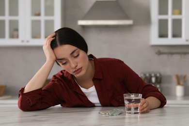 Photo of Depressed woman with glass of water and antidepressant pills at white marble table in kitchen