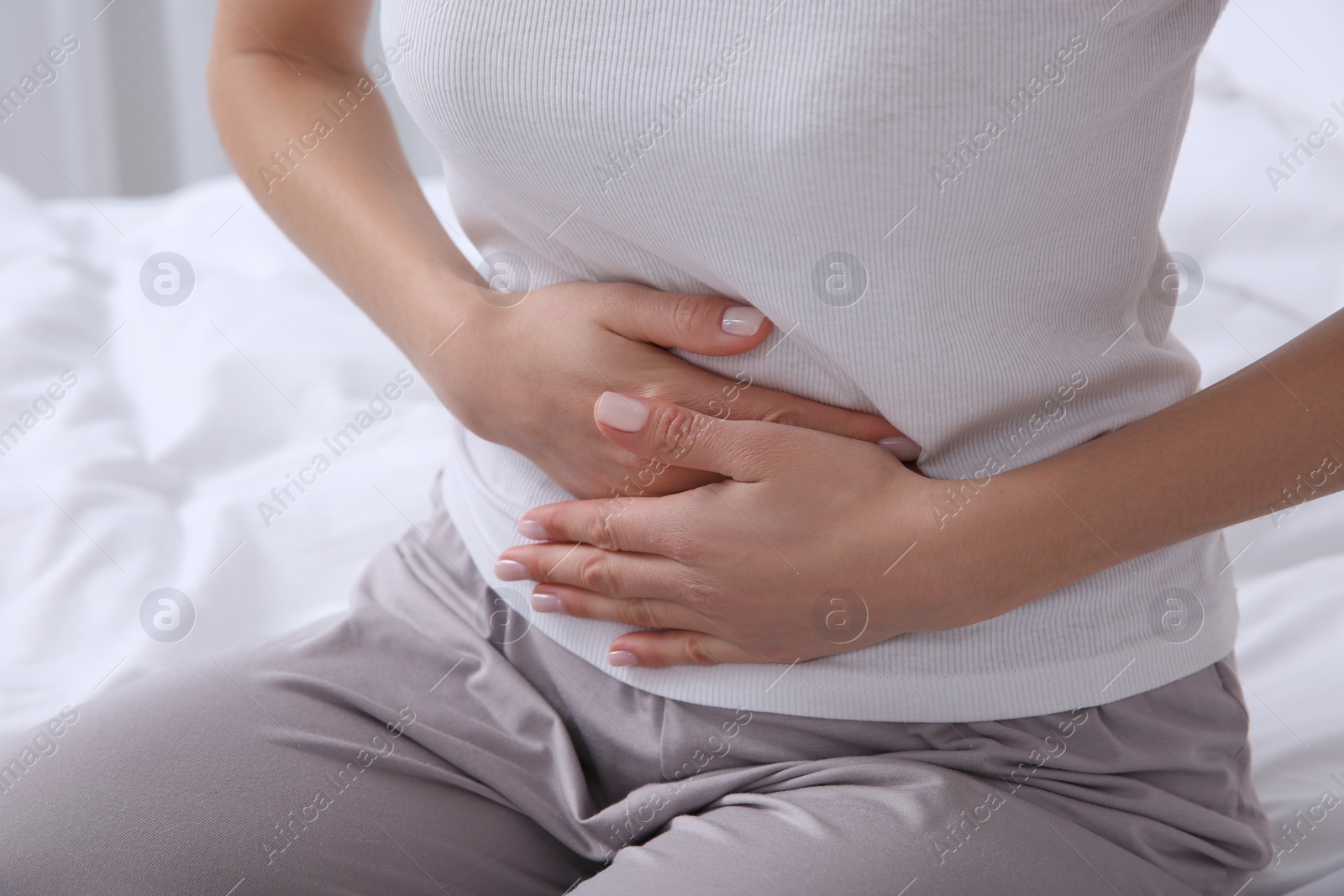 Photo of Young woman suffering from stomach ache on bed, closeup