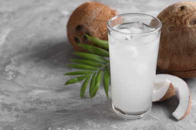 Glass of coconut water with ice cubes, palm leaf and nuts on grey table. Space for text