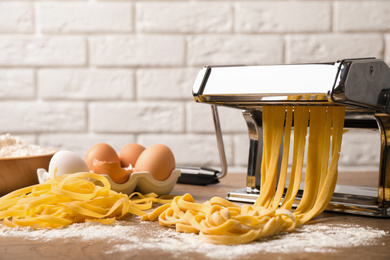 Photo of Pasta maker machine with dough and products on wooden table against brick wall