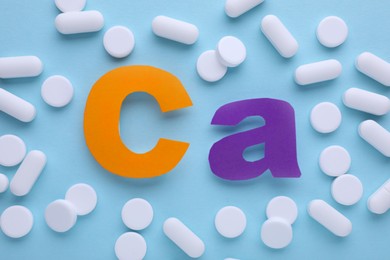 Photo of Calcium symbol made of colorful letters and white pills on light blue background, flat lay