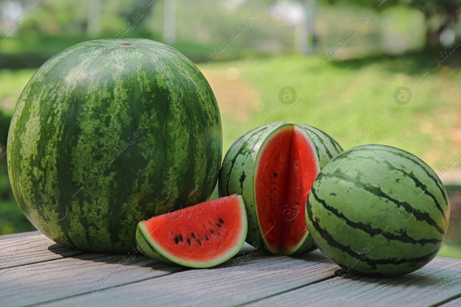 Photo of Different ripe whole and cut watermelons on wooden table outdoors