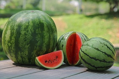 Photo of Different ripe whole and cut watermelons on wooden table outdoors