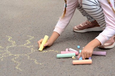 Photo of Little child drawing sun with chalk on asphalt, closeup