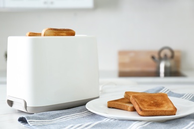Modern toaster with slices of bread on table in kitchen