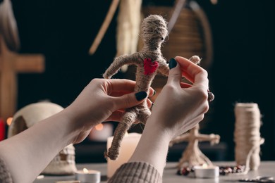 Photo of Woman pricking voodoo doll's heart with pins at table, closeup