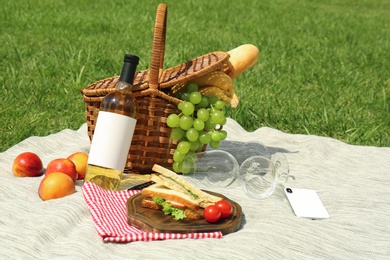 Photo of Basket with food and wineglasses on blanket prepared for picnic in park