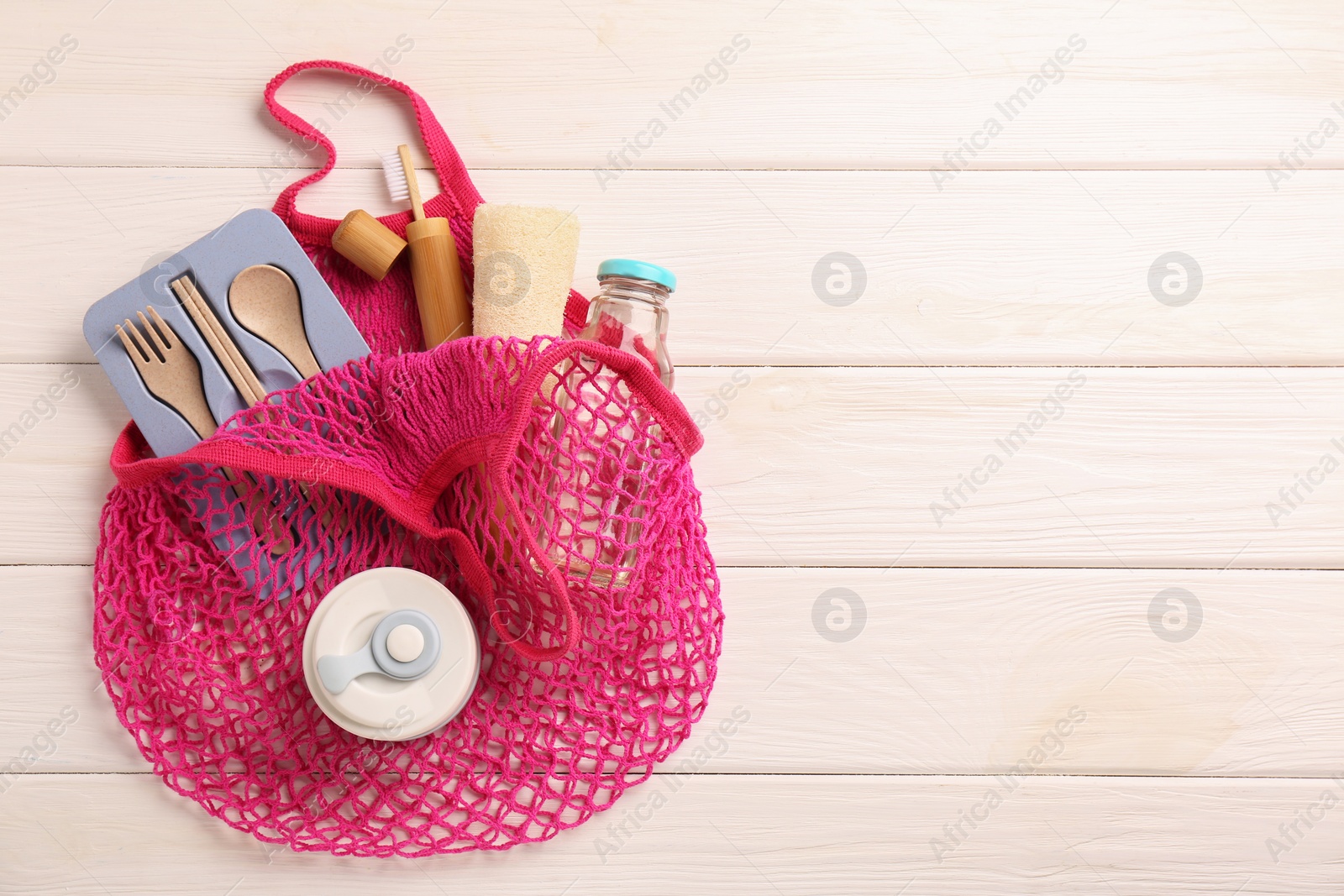 Photo of Net bag with different items on white wooden table, top view and space for text. Conscious consumption