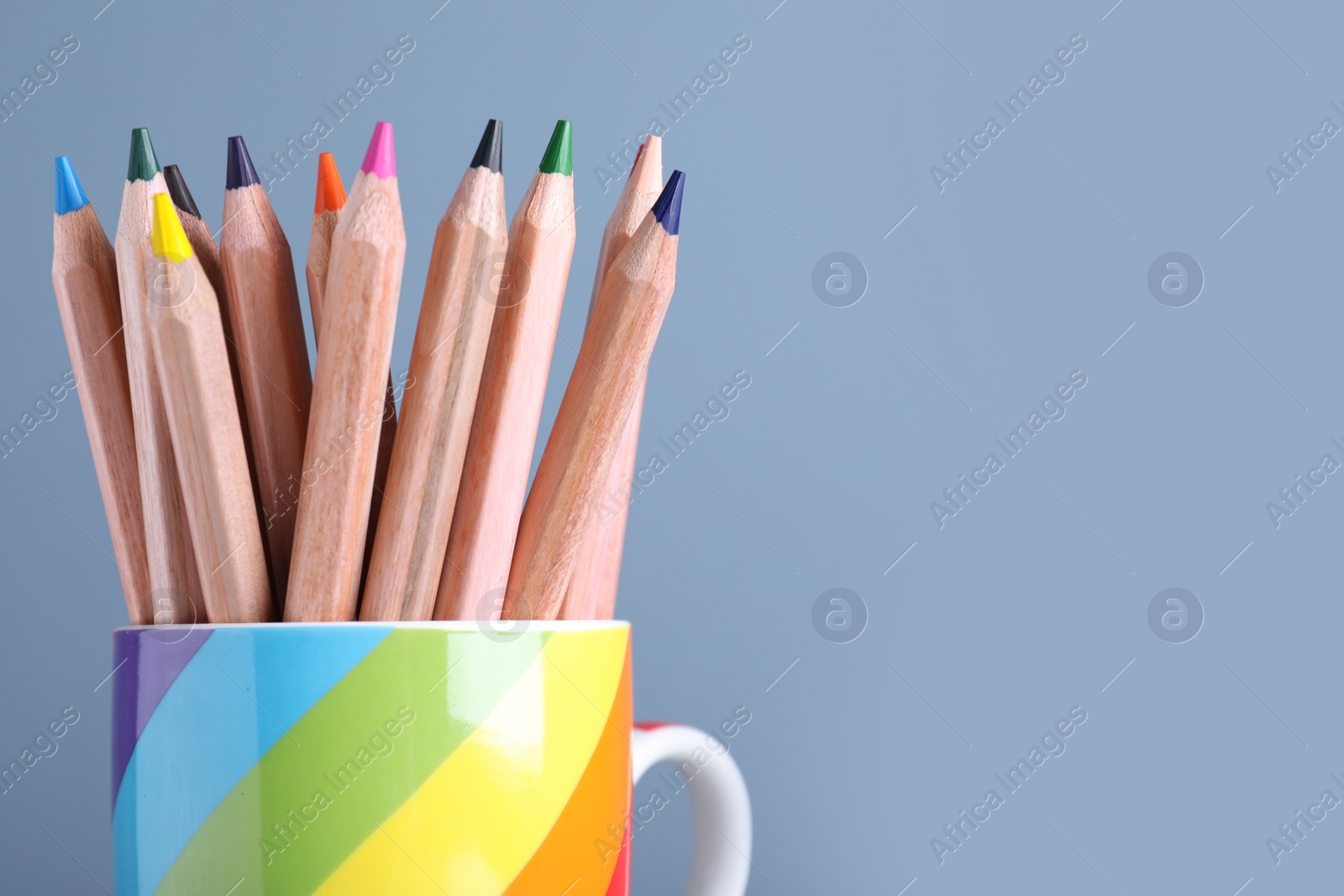 Photo of Colorful pencils in cup on light blue background, closeup. Space for text