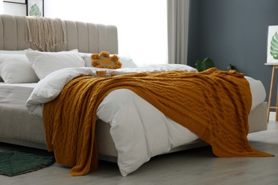 Photo of Comfortable bed with knitted orange plaid in stylish room interior