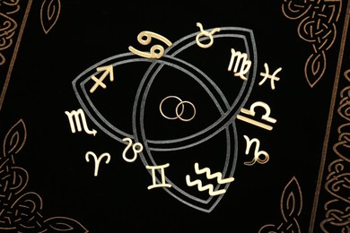 Photo of Zodiac signs and wedding rings on book, flat lay