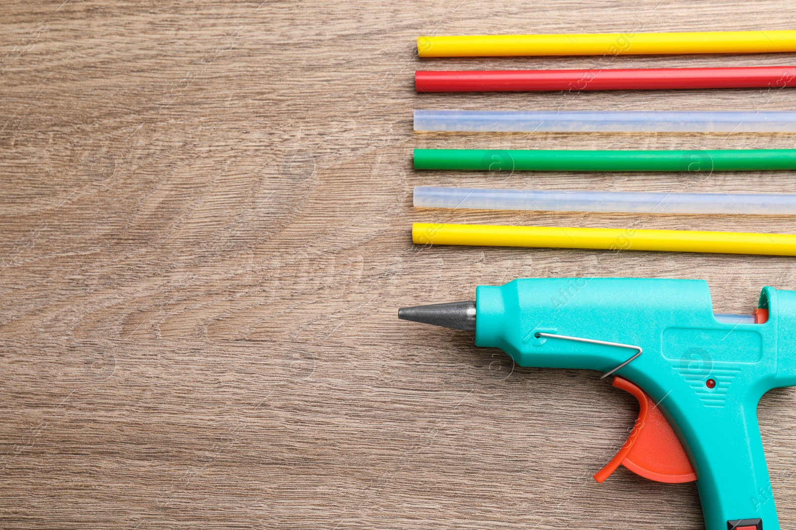 Photo of Turquoise glue gun and colorful sticks on wooden table, flat lay. Space for text