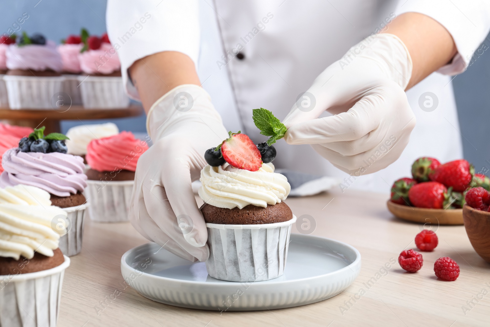 Photo of Pastry chef decorating sweet cupcake with mint at light wooden table, closeup