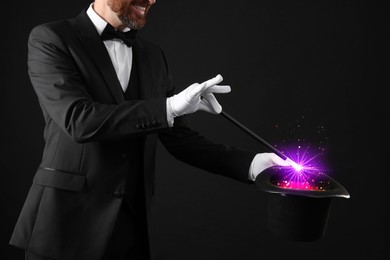 Image of Magician showing trick with wand and top hat on dark background, closeup. Fantastic light coming out of hat