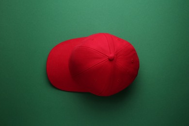 Photo of Stylish red baseball cap on green background, top view