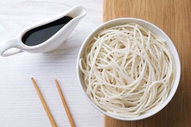 Bowl of rice cooked noodles and soy sauce served on white wooden table, flat lay