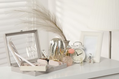 Photo of Jewelry boxes with many different accessories, perfumes, alarm clock and decor on white wooden table indoors