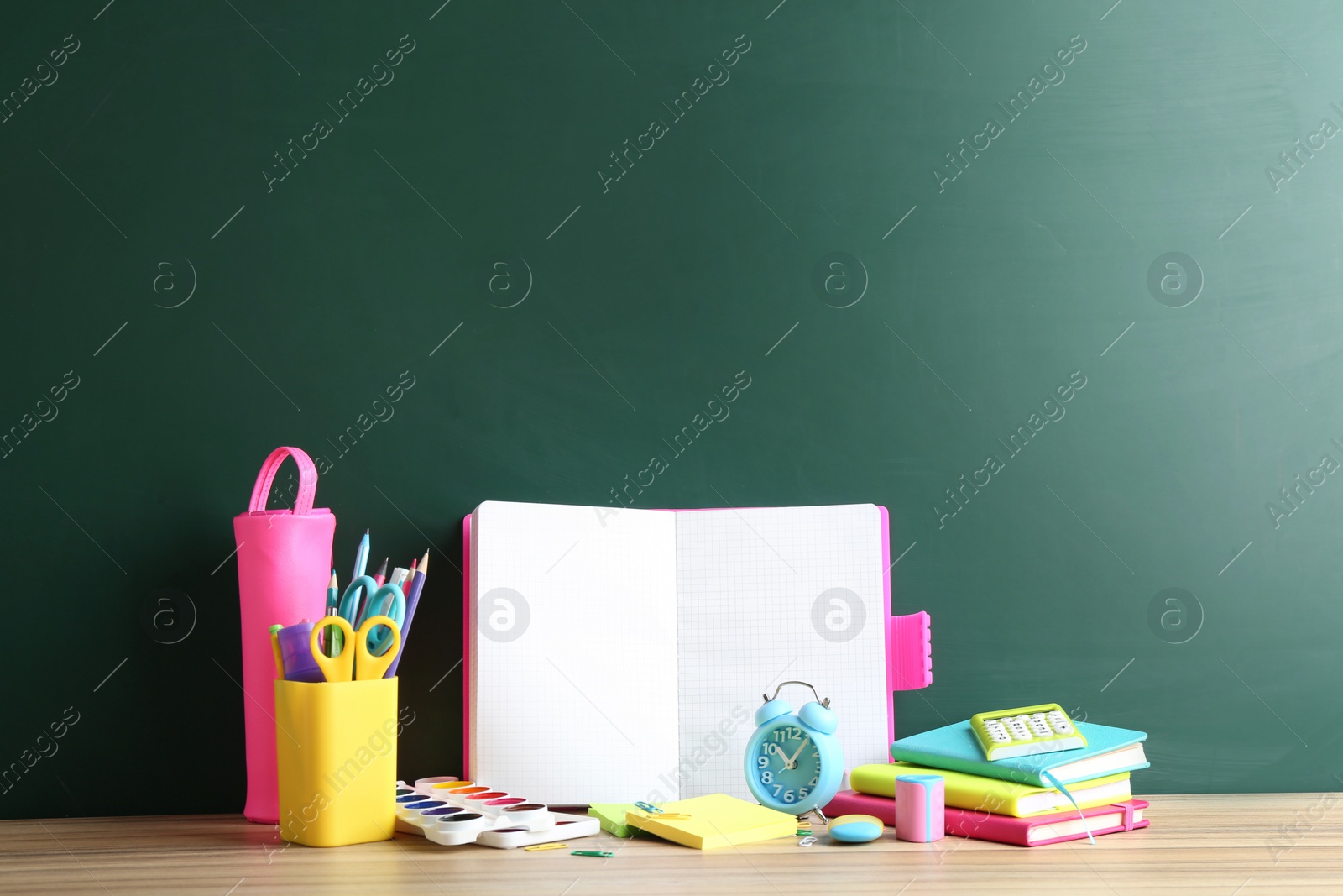 Photo of Different school stationery and blank notebook on table near chalkboard. Space for text