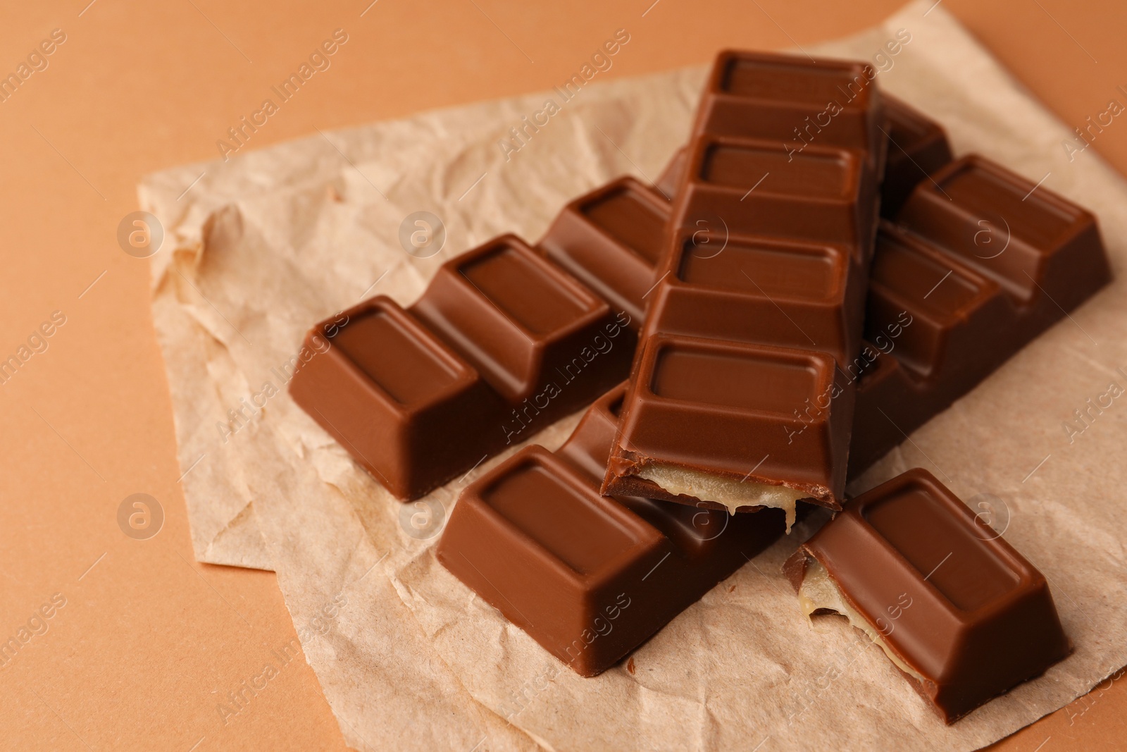 Photo of Parchment with delicious chocolate bars on light brown background, closeup