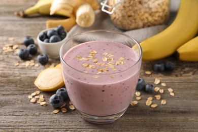 Photo of Glass of tasty banana blueberry smoothie with oatmeal on wooden table