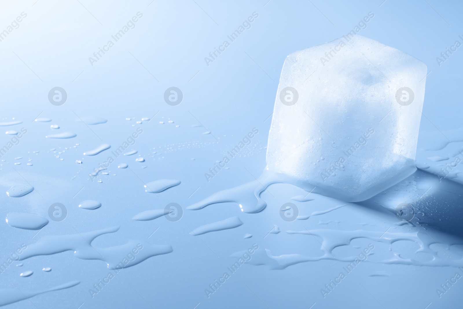 Photo of Crystal clear ice cube on light blue background, space for text