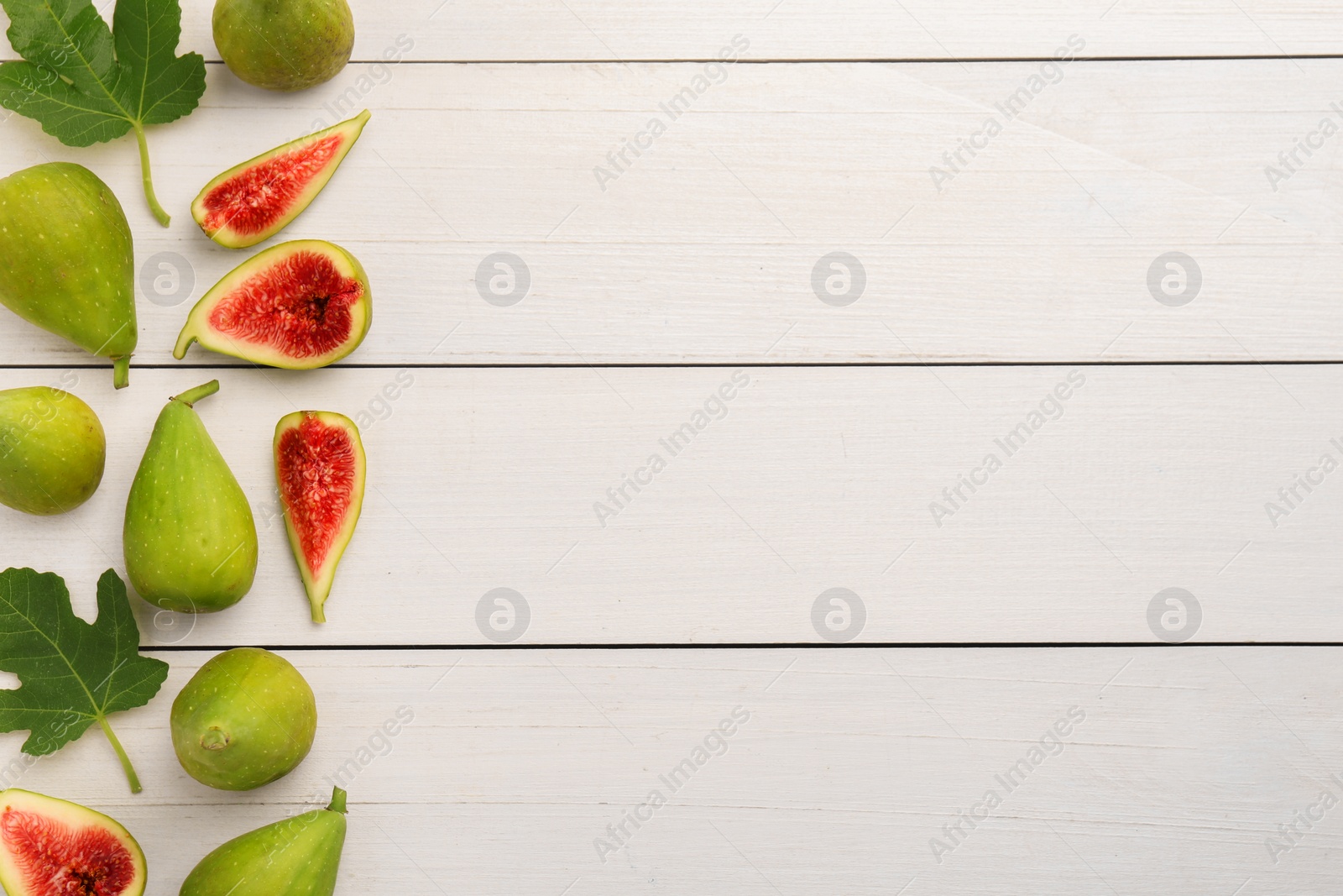 Photo of Cut and whole green figs with leaves on white wooden table, flat lay. Space for text