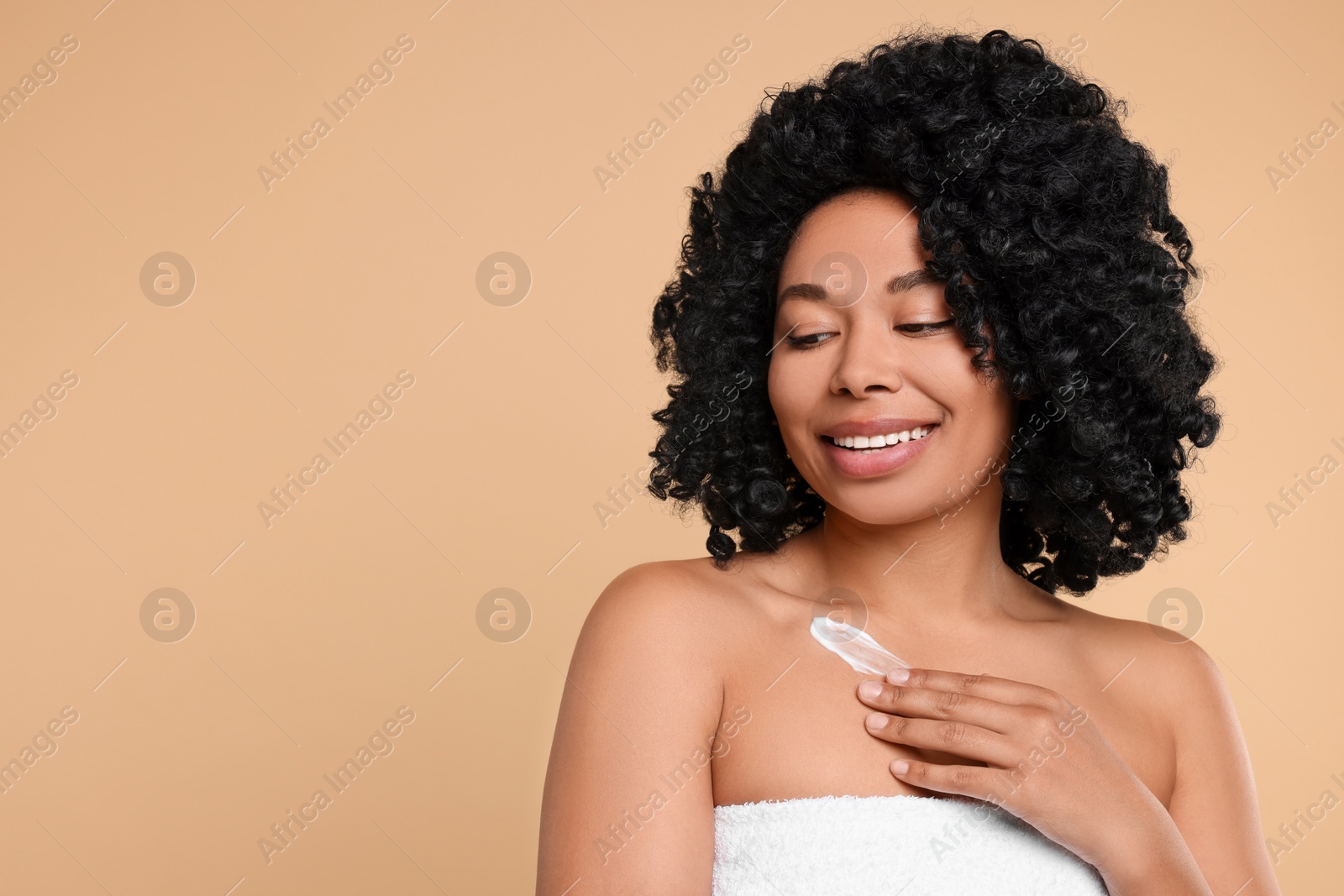 Photo of Young woman applying cream onto body on beige background. Space for text