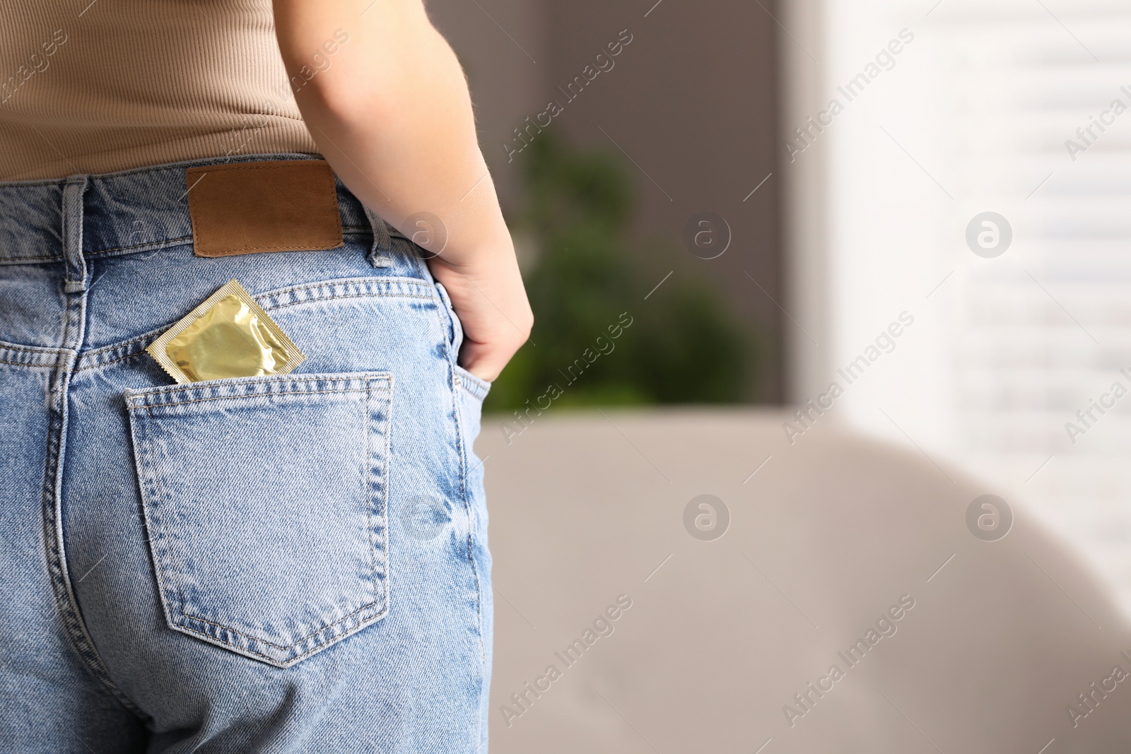 Photo of Teenage girl with condom in pocket of her jeans indoors, closeup. Sex education concept