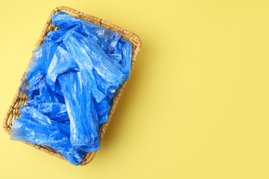 Photo of Blue medical shoe covers in wicker basket on yellow background, top view. Space for text