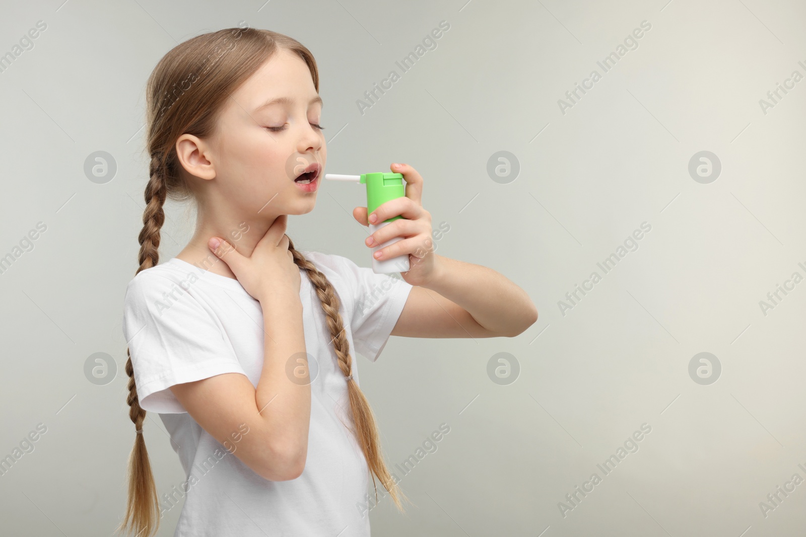Photo of Little girl using throat spray on light grey background. Space for text