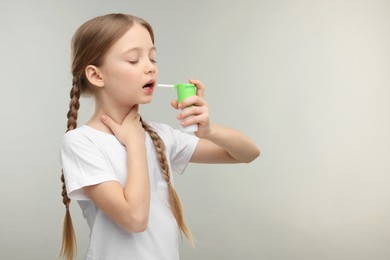 Little girl using throat spray on light grey background. Space for text